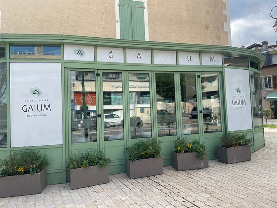 Façade du Restaurant Gaium au Pays de Gex, avec de grandes fenêtres et des jardinières fleuries, créant une entrée accueillante et élégante.